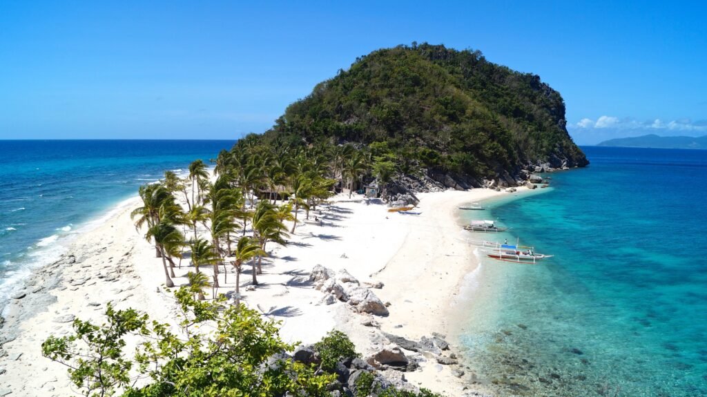 Stunning aerial view of Isla de Gigantes, featuring crystal-clear turquoise waters, white sandy beaches, and lush green cliffs in Iloilo, Philippines.